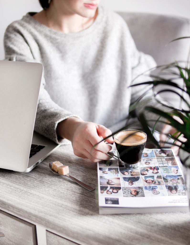 A person holding a cup of coffee on a desk next to a laptop